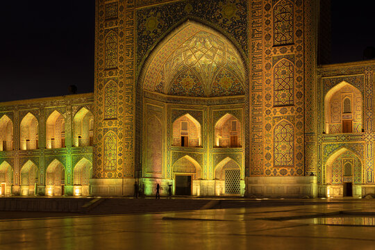 Illuminated Tilla-Kari madrasah facade at Registan Square in Samarkand at night with intricate tilework, golden lighting. Ideal for travel publications, cultural heritage content, tourism brochures.