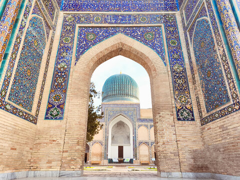 Gur-e-Amir mausoleum portal and turquoise dome in Samarkand, Uzbekistan. Ornate tilework and brick archway frame the iconic Timurid monument. Ideal for travel guides, cultural publications.