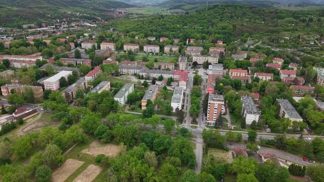 An aerial drone perspective captures a residential neighborhood with apartment blocks integrated into a lush, green spring landscape in Europe.
