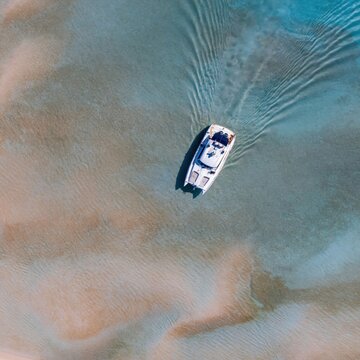 Transparent turquoise coastal sea water with a luxury motor boat cruising above a sandy seabed for summer vacation advertising, yacht charter marketing and travel web background