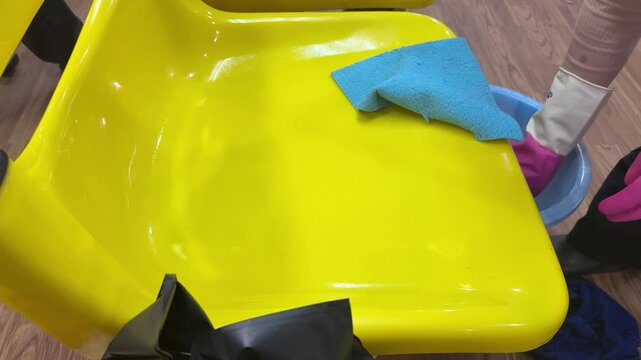 Cleaning staff are wiping down yellow chairs with cloths and spraying them with disinfectant at the hospital.