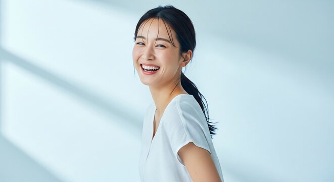 Young Asian woman with dark hair pulled back smiling joyfully wearing a white v neck shirt studio lighting