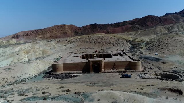 Stone caravanserai ruins nestled among rocky hills in arid desert under bright blue sky creating integrated historical landscape scene perfect for archaeology and travel stock video footage.