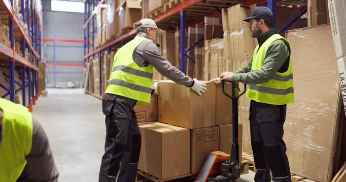 Workers in warehouse loading boxes onto pallet. Team coordinates manual delivery with trolley among racks, preparing goods for shipping and storage. Strong teamwork and logistics concept.