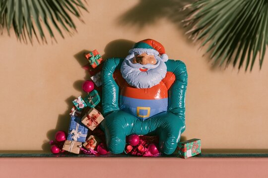 Teal inflatable Santa Claus float sitting by a pool with gift boxes for tropical holiday marketing, winter sun advertising and seasonal hospitality background