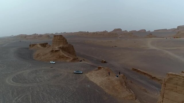 Wide desert landscape features multiple yardang rock formations eroded by wind under hazy sky with flat terrain stretching to horizon creating dramatic natural erosion vista perfect for geology and