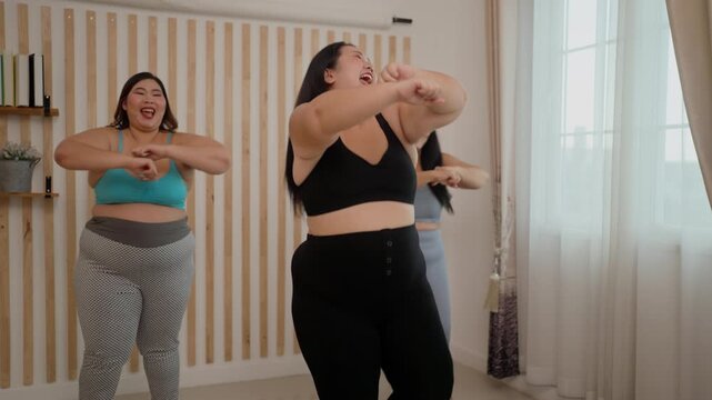A group of three plus-size girls in a room are having fun exercising together.
