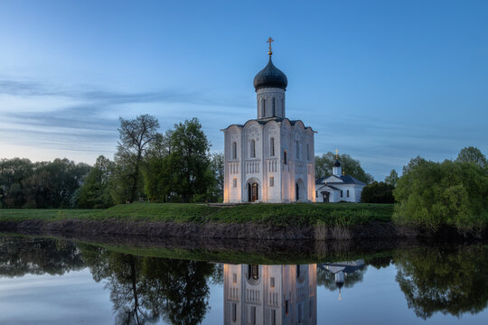 Historic Church of the Intercession on the Nerl reflected in calm river water at sunset, famous white stone Orthodox church near Vladimir and Suzdal, Russia, scenic spring landscape with dramatic sky.