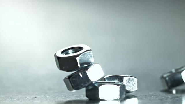 Closeup hex nuts and fasteners on reflective table, staged stack falls Filmed on a high-speed camera at 1000 fps.