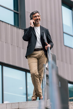 Cheerful mature businessman talking on the phone while walking through the city.