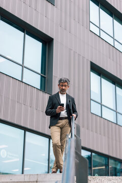 Mature elegant businessman using smartphone while walking through the city.