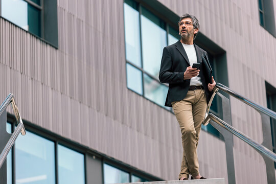 Mature elegant businessman using smartphone while walking through the city.