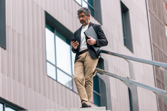 Mature elegant businessman using smartphone while walking through the city.