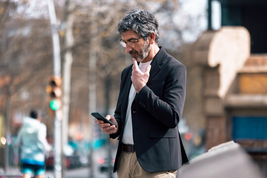 Mature elegant businessman using smartphone while walking through the city.