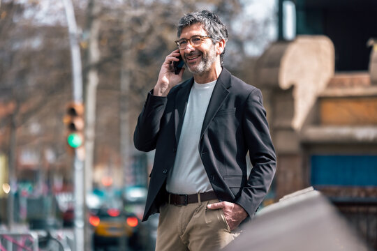Cheerful mature businessman talking on the phone while walking through the city.