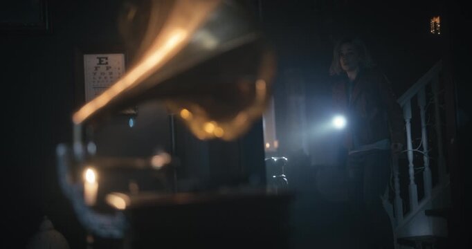 Record turns on turntable of gramophone as nervous woman with flashlight looks around dark home