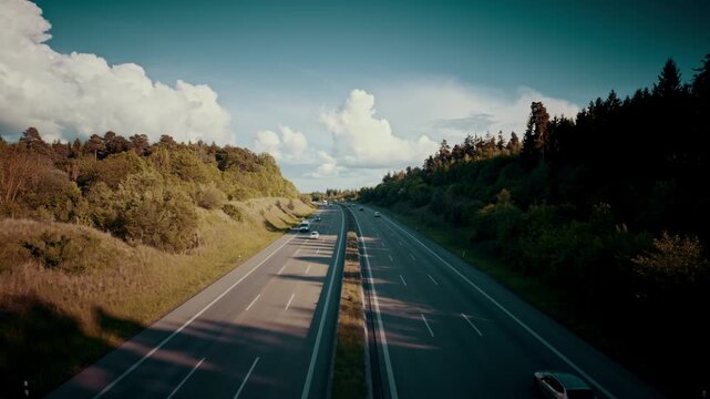 A high-angle view of a highway cutting through a green landscape where one side is congested with a long line of cars and trucks, while the other side flows freely under a cloudy sky.