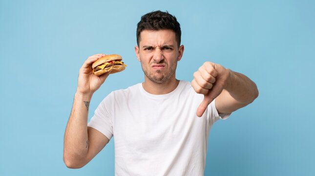 Man with a displeased expression holding a burger and giving a thumbs down gesture fast food junk food not good