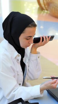 Woman In Hijab Recording Voice Memo While Using Tablet, Holding Smartphone To Mouth, Gesturing With Free Hand,