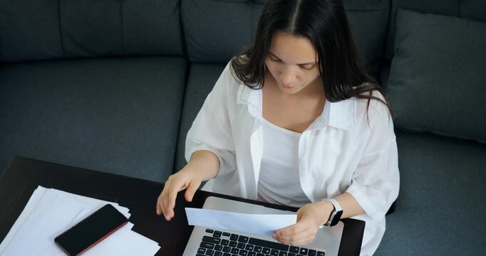 Woman handles accounting. Female reviews bills diligently. Woman sorts and examines financial documents carefully. Household woman organizes invoices and receipts on workspace table