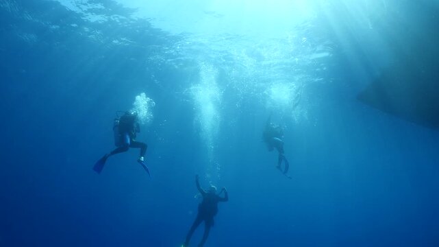 scuba divers ascending surface going back to boat underwater with sun beams and rays ocean scenery