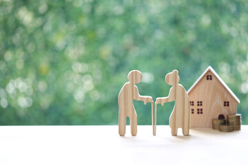 Couple wooden figures standing with a miniature house and coins, representing retirement home planning, property investment, real estate for seniors and financial security for old age. © Monthira