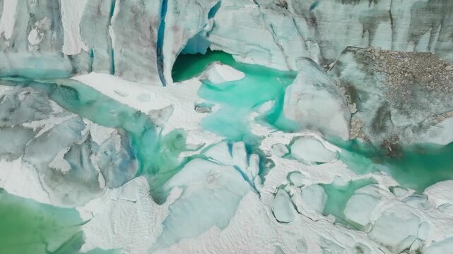 Drone flies closely toward a dramatic ice cave and turquoise emerald glacier pool surrounded by crevasses, ice rocks, and rugged frozen landscapes.