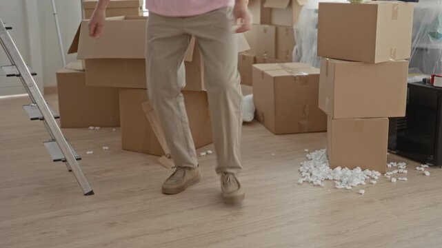 Man stepping among cardboard boxes and scattered packing peanuts while carrying a small package in a building; anticipation transition.