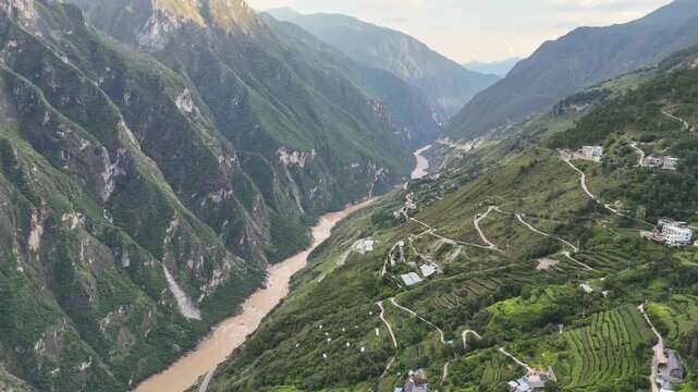 Cinematic aerial shot of the deep Tiger Leaping Gorge canyon featuring the Jinsha River and winding mountain trails. Suitable for travel documentaries and adventure content.