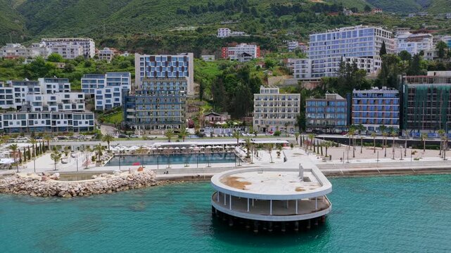 Aerial video capturing the rugged southern coastline of Vlora, Albania, highlighting a unique circular overwater pier structure
