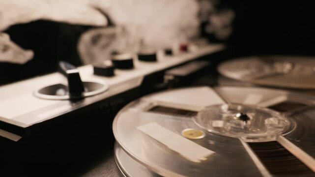 A vintage reel-to-reel audio tape recorder operates in a dark studio. Thick white smoke billows over the spinning spools and control knobs. The retro analog equipment creates a moody
