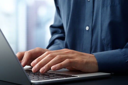 Businessman using laptop computer at desk in office. Closeup of hands and keyboard. Business technologies.