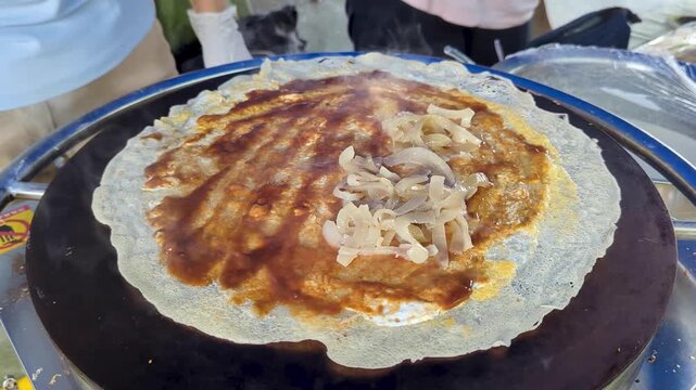 Adding savoury ingredients on crepe cooking on steaming hotplate at local market in Suva, Fiji