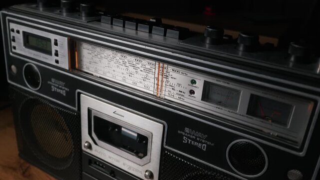 Detailed close up view of a classic vintage boombox stereo system featuring an illuminated analog tuning dial, buttons, and cassette deck. This visualizes a retro audio technology concept.