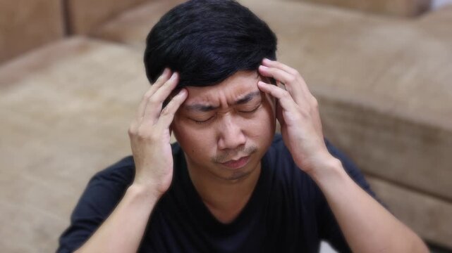 A man in a black shirt holds his head and rubs his temples, showing severe headache pain