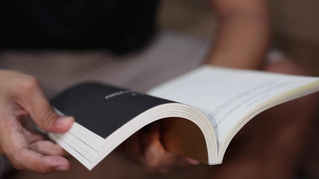 A close-up shot of a person casually sitting and flipping through the pages of a book