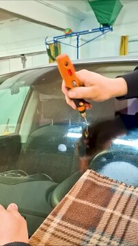 Professional mechanic drilling a car windshield crack using a rotary tool close up, automotive glass repair and restoration process in auto service.