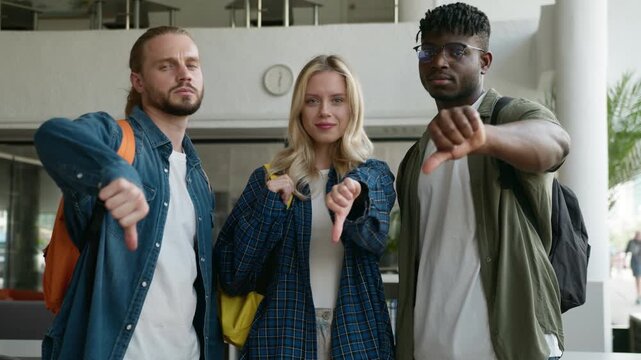Three diversity students posing showing thumbs down no reject deny gesture in university college denied sign bad exam result multiracial classmates multiethnic friends looking at camera in academy