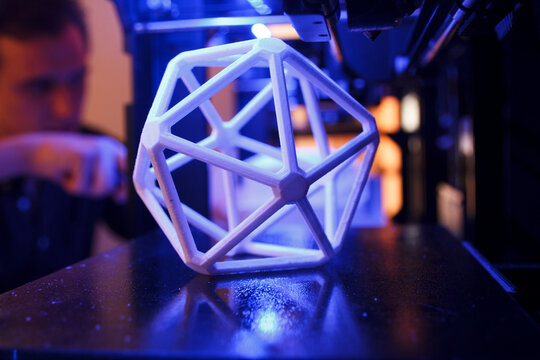 3D geometric figure on the platform of a 3D printer with a man in the background
