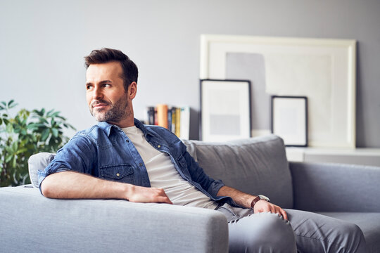 Smiling relaxed man sitting on sofa looking away