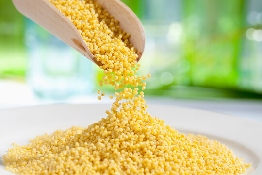 Millet seeds pouring from wooden scoop, close up