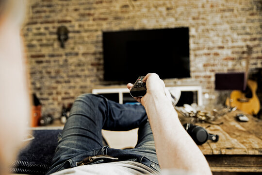 Man lying on the couch using remote control, partial view
