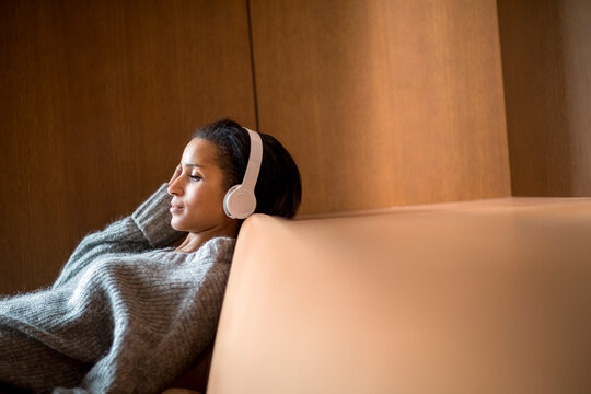 Portrait of relaxed young woman listening music with headphones on couch