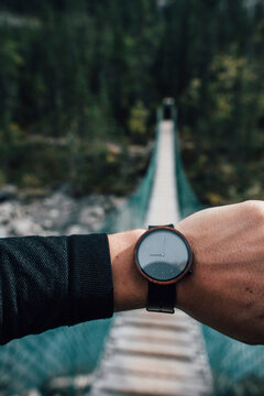 Man's hand with watch in front of swinging bridge