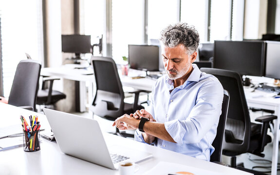 Mature businessman sitting at desk in office looking at smartwatch