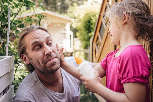 Daughter applying sunscreen on father's face in garden