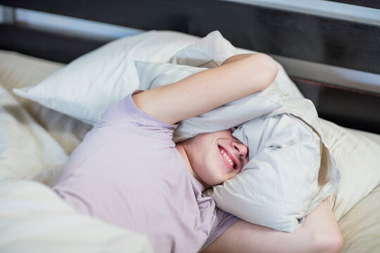 Boy lying in bed holding pillow over his head
