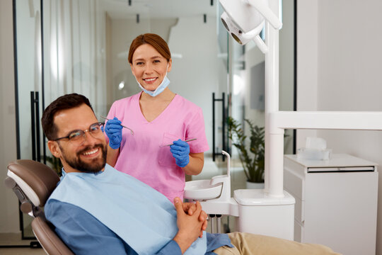 Dentist holding instruments with a male patient sitting in a dental chair smiling