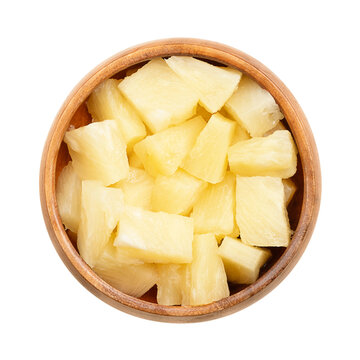 Canned pineapple chunks, in a wooden bowl. Ripe pineapples, cut into block shaped pieces, boiled in its own juice, and then tinned. Isolated, close-up, from above, on white background, food photo.