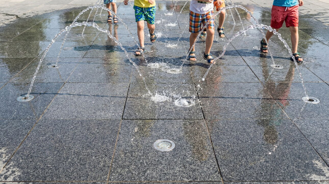 Children playing in water fountain jets on granite pavement summer fun, running.